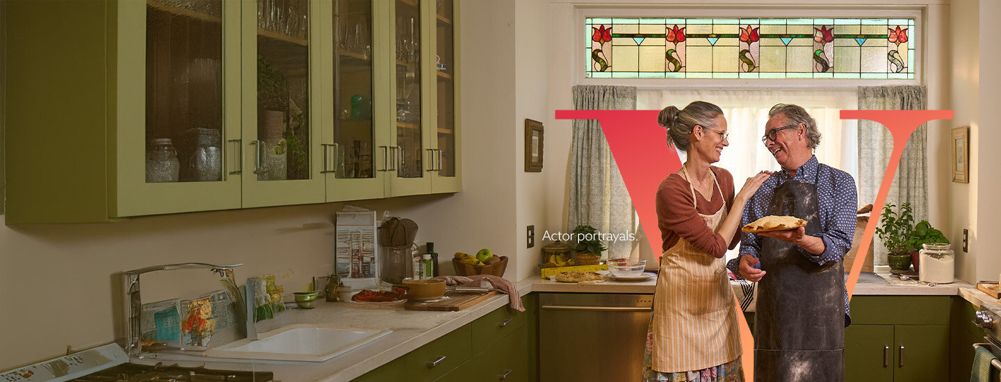 A woman and a man in a kitchen laughing while holding food